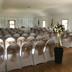 Ceremony set out with rows of chairs with white chair covers and gold bows